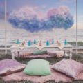 cotton candy clouds hang over a picnic style table with cushions on the beach