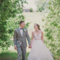 bride and groom hold hands while walking through sunny filed of trees