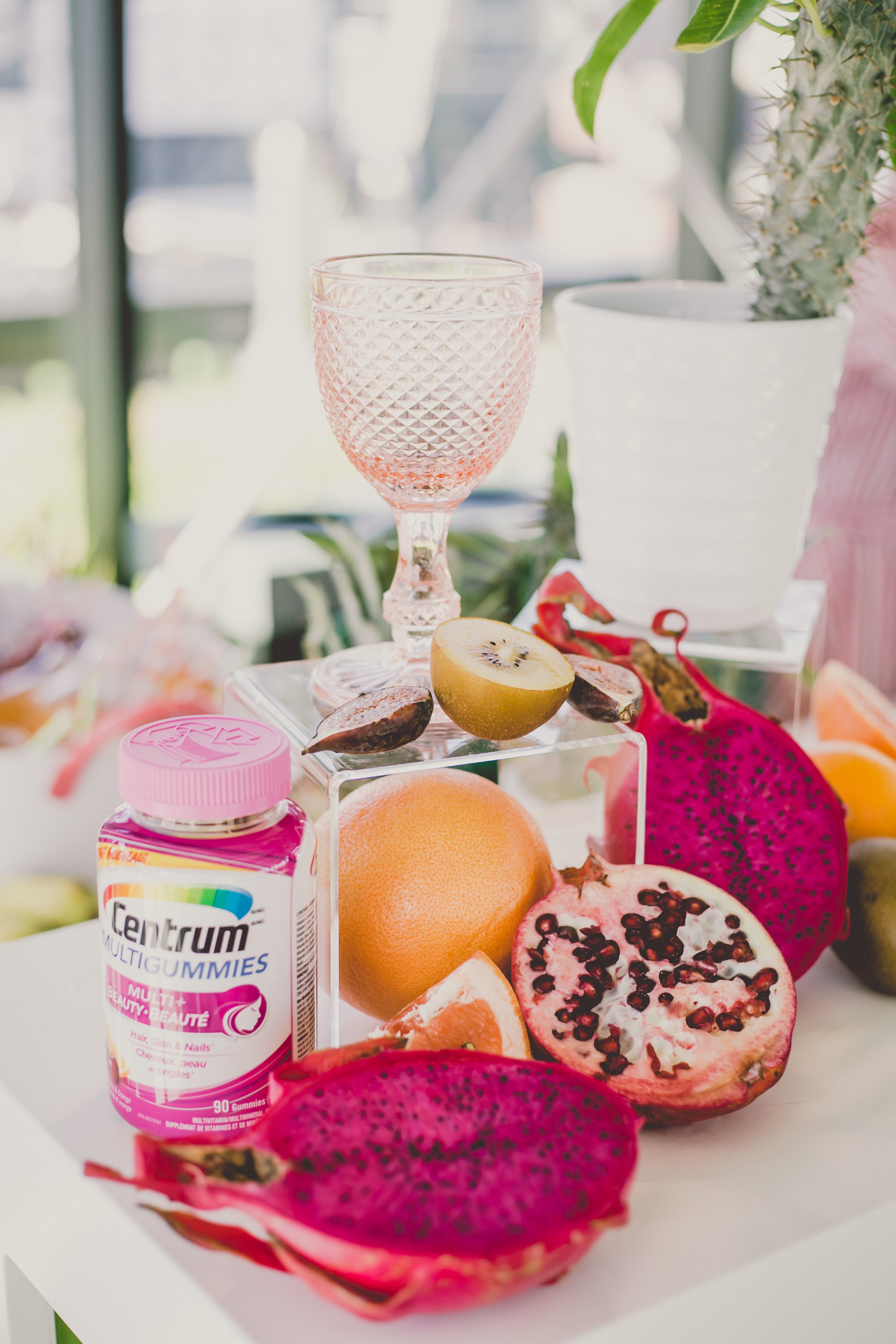 Pink Centrum multivitamins surrounded by vitamin rich foods like grapefruits, pomegranates, and pink dragonfruit. 