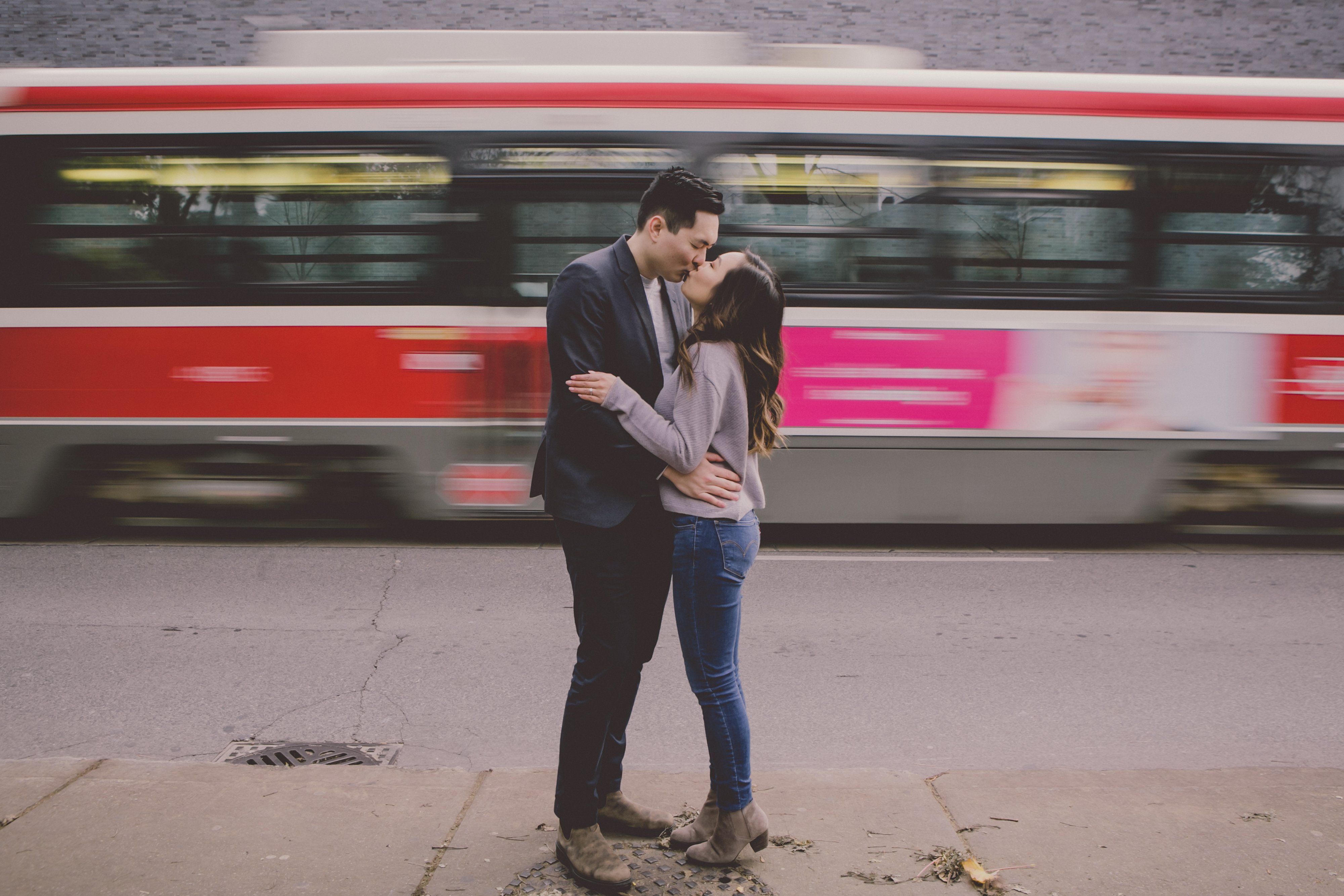 Liane & Victor, an engaged couple, kiss while a streetcar zooms by in the background. 