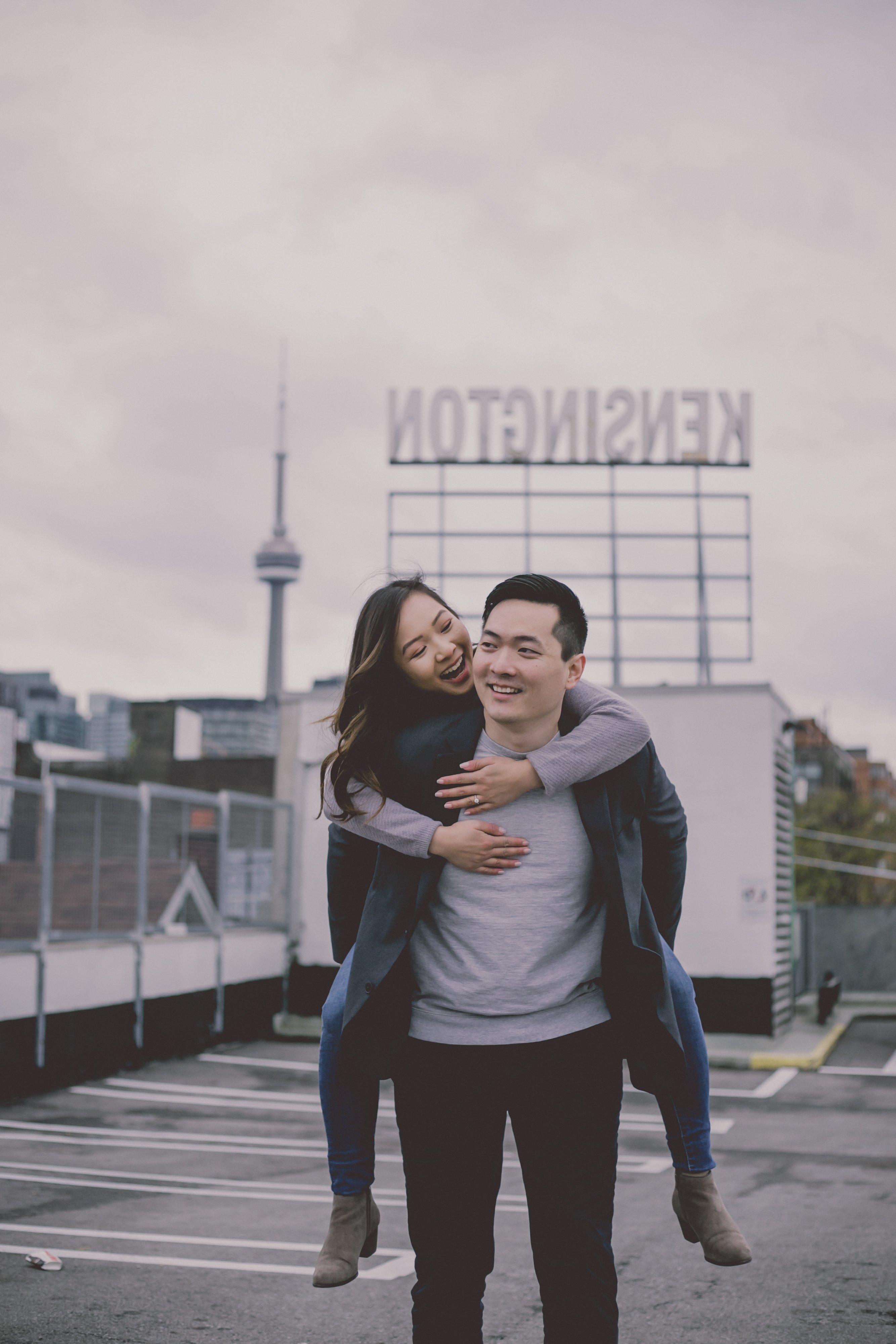 Engaged couple playing piggyback on a rooftop in Kensington Market in downtown Toronto while being photographed by Olive Studio Photography. 