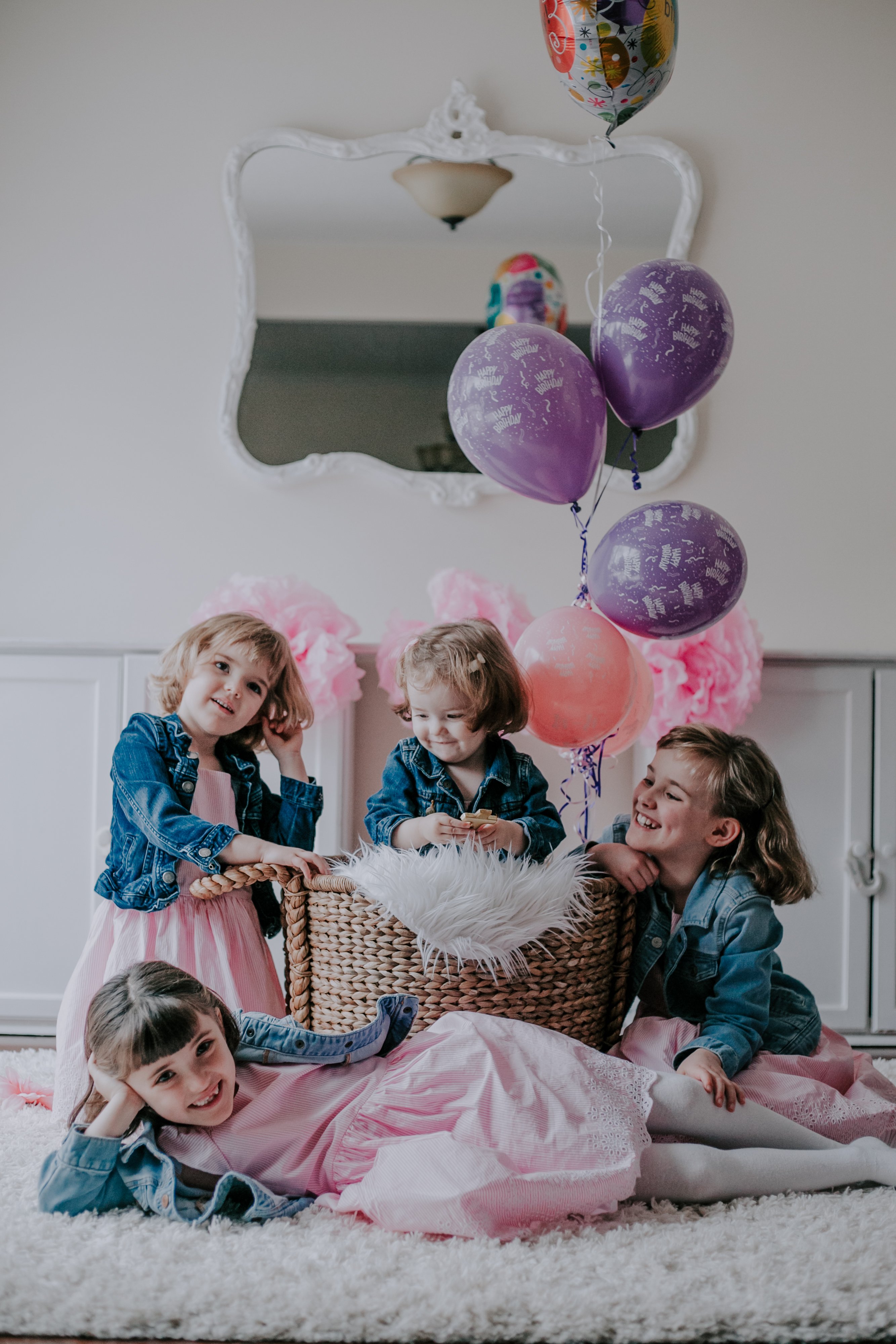 Josie and her three older sisters during her Cake Smash Session in Toronto. The birthday girl sits in a wicker basket with helium balloons attached looking like she'll be carried away Up style if her sisters stop leaning on the basket!