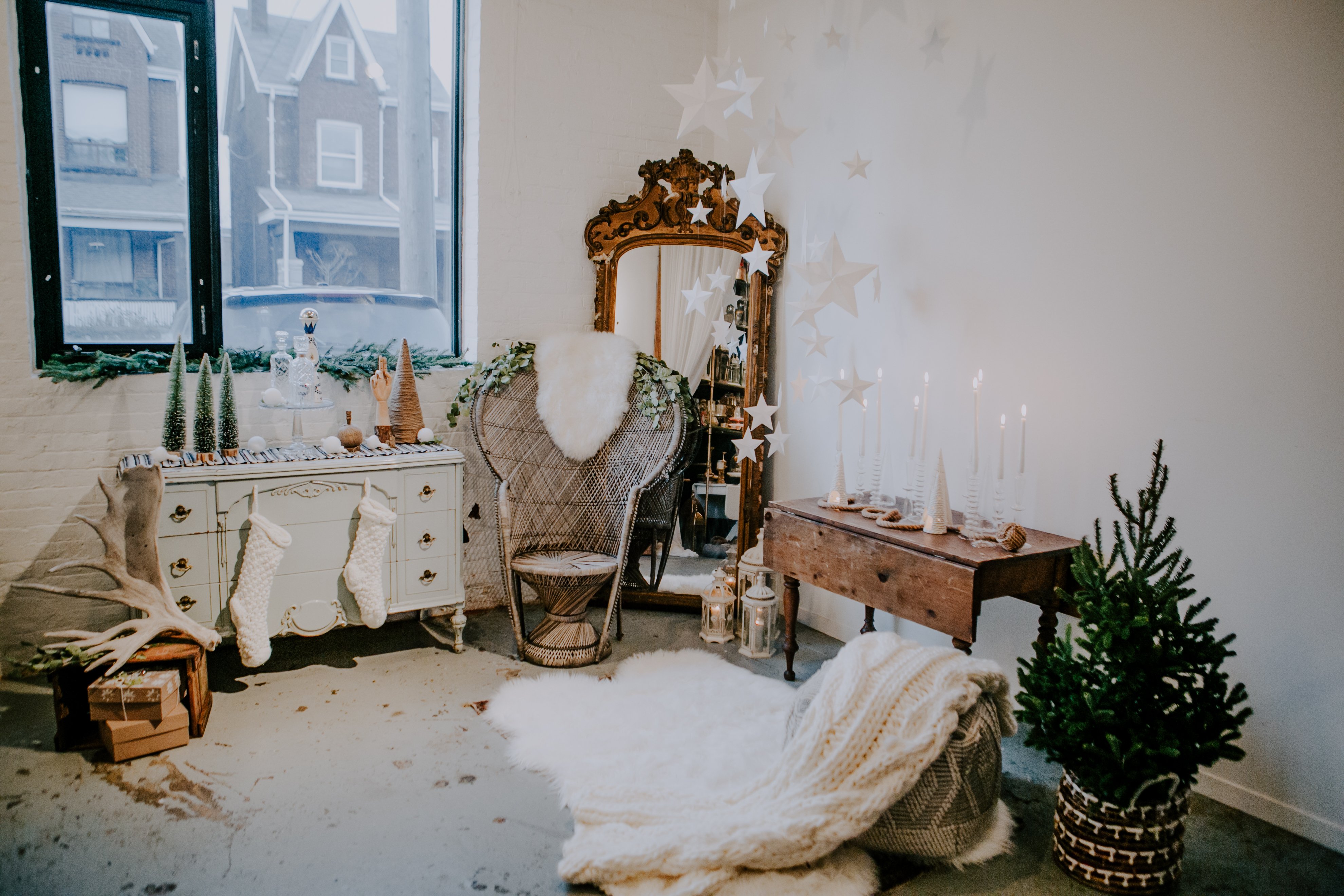 A white paper star installation hangs from the room of Olive Studio surrounded by a small fern tree, a vintage mirror in the corner, and faux fir throws and white knit stockings draping the furniture. 