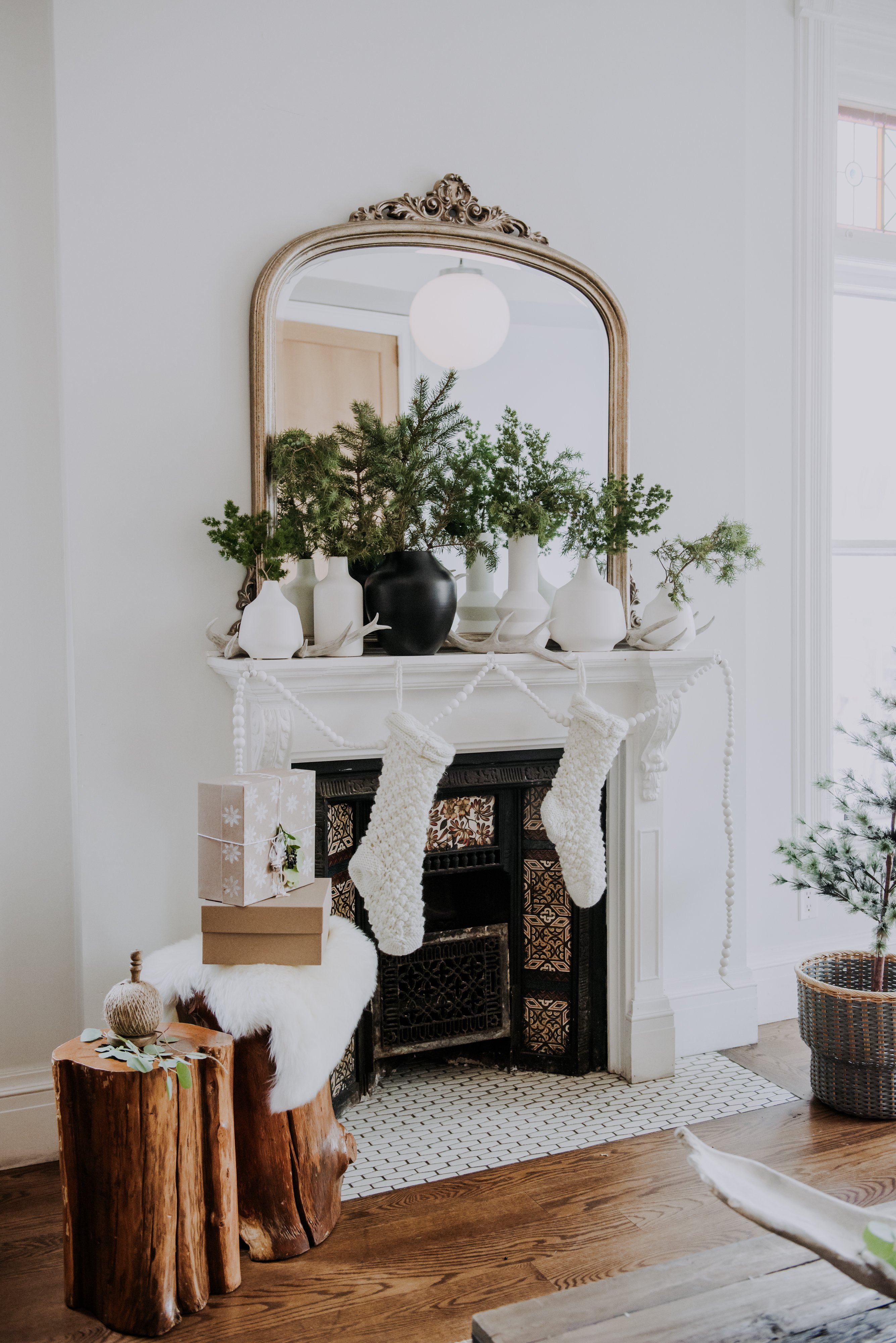 The fireplace mantle at Peter Pan Bistro is styled with giant white stockings, white ceramic plant holders of different shapes and sizes all containing pine branches and a single black plant holder as part of Reitmans' Holiday Brand Activation Brunch styled by Olive Studio. 