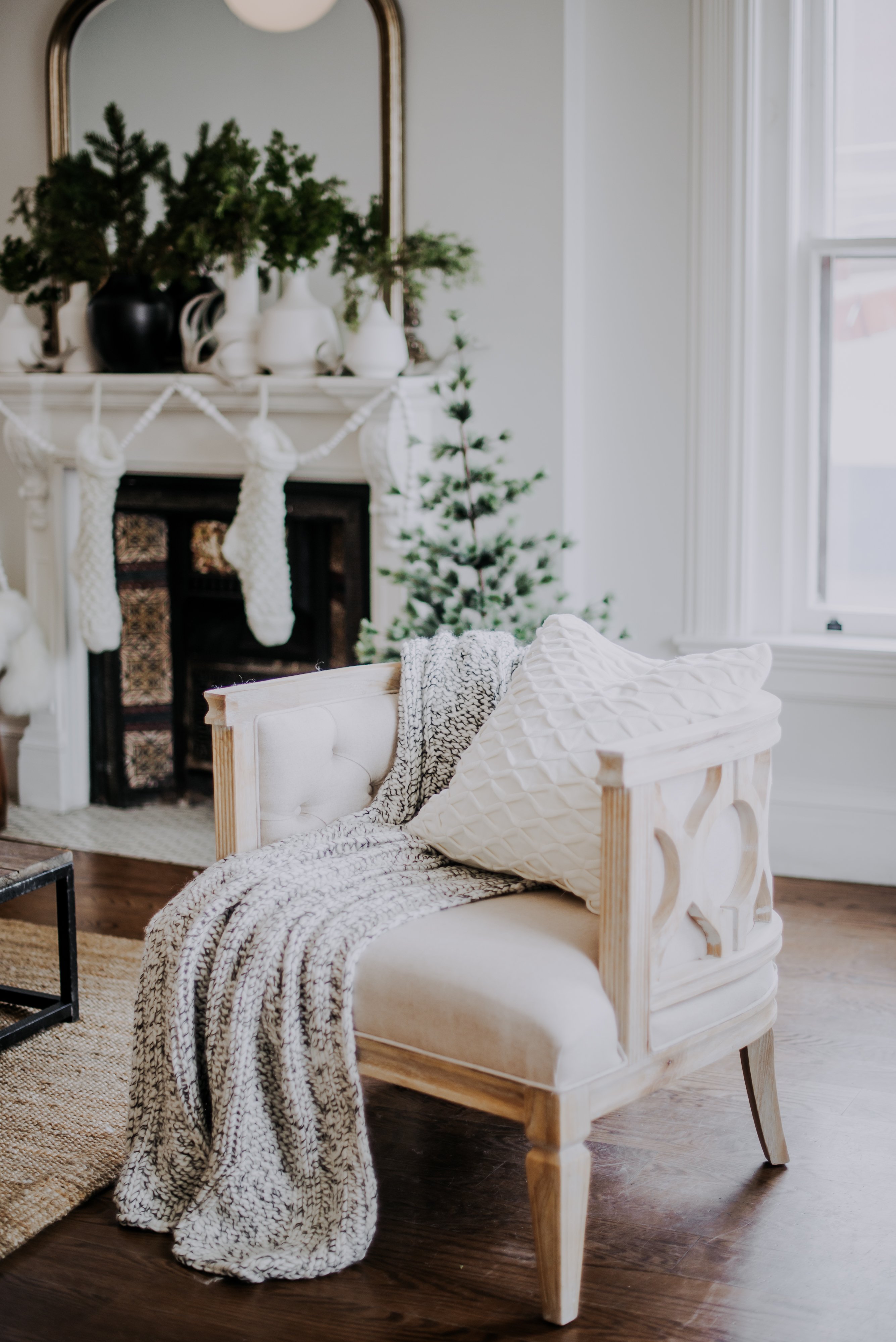 A soft white Belgian accent chair with a pale gray knit throw and textured white pillow on top at the Scandinavian holiday inspired Reitmans Holiday Brand Activation styled by Olive Studio in Toronto. 