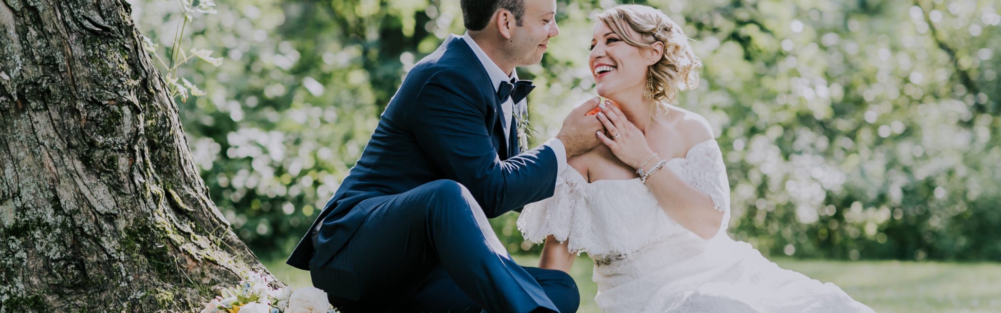 bride and groom sit on grass laughing