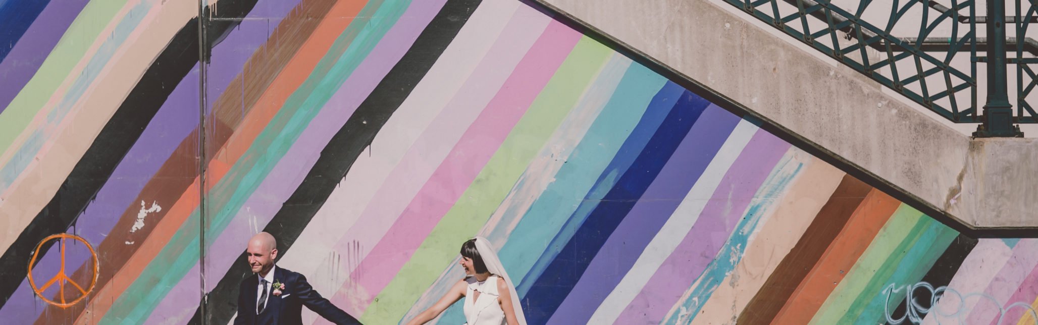 groom leads bride down sidewalk in front of graffiti wall in Roncesvalles.