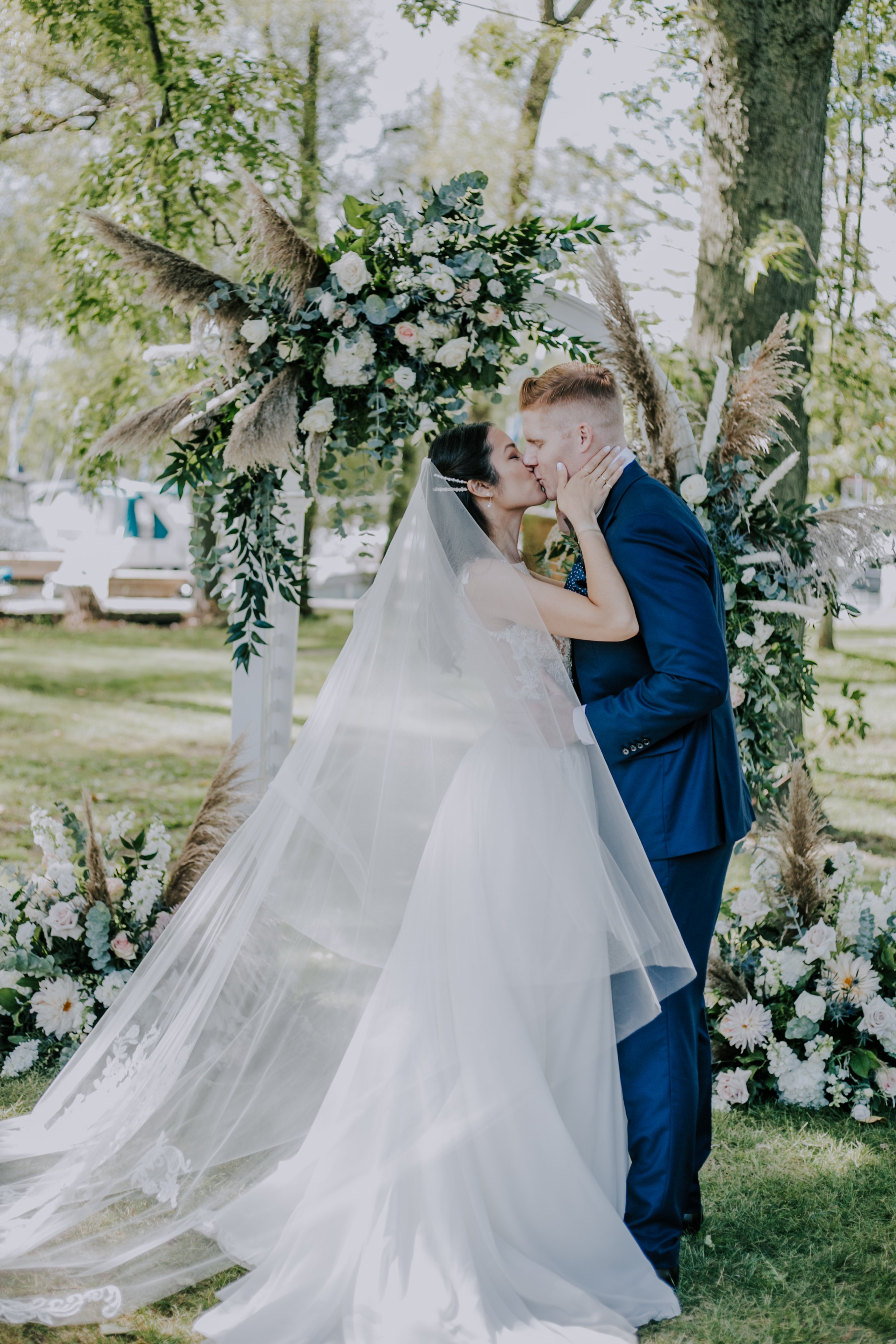 asian girl and white man kiss in front of an outdoor altar covered with flowers and pampas grass