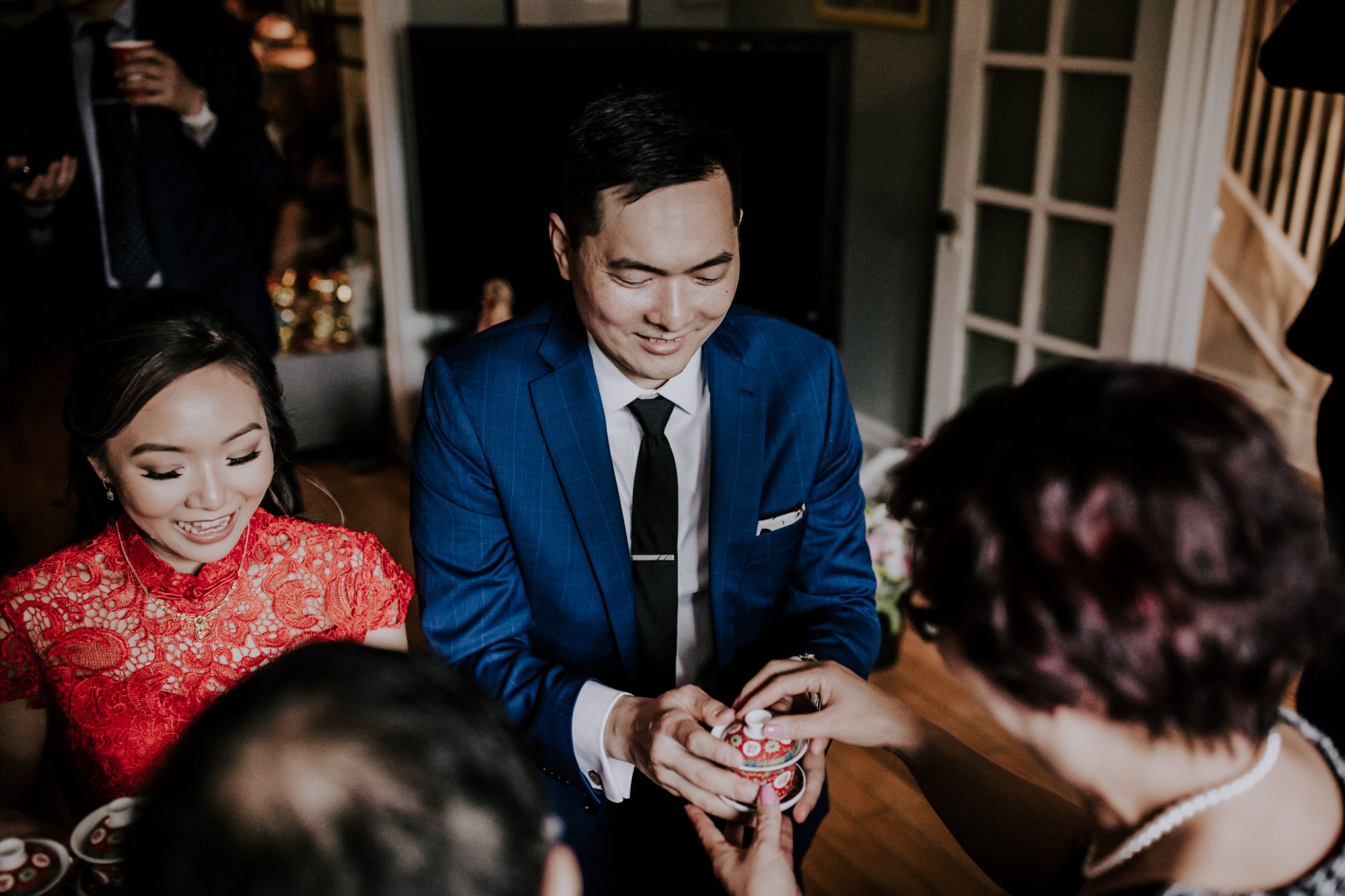 groom passes tea cup to mother during chinese tea ceremony