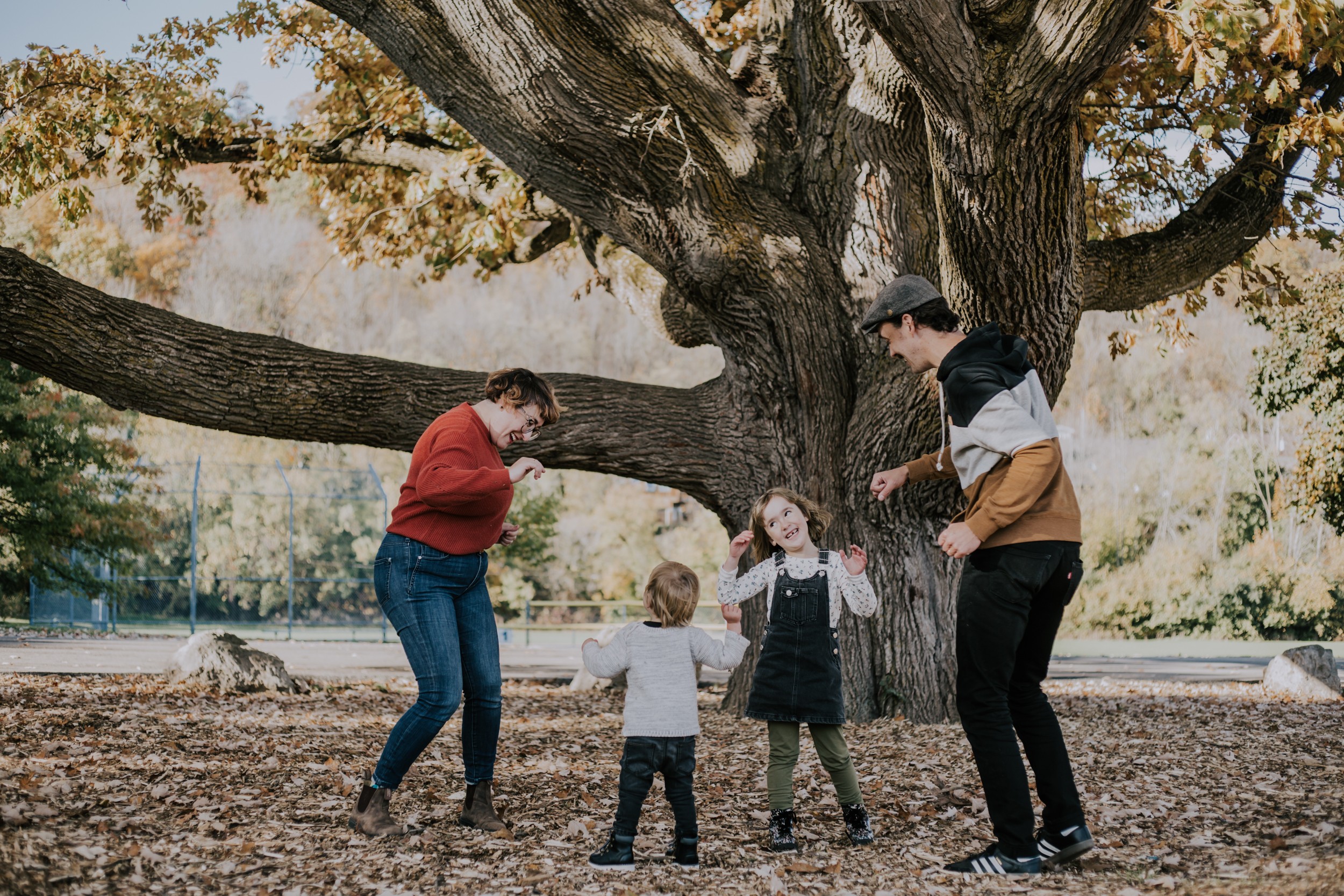 mother, father and two small kids dance under a tree