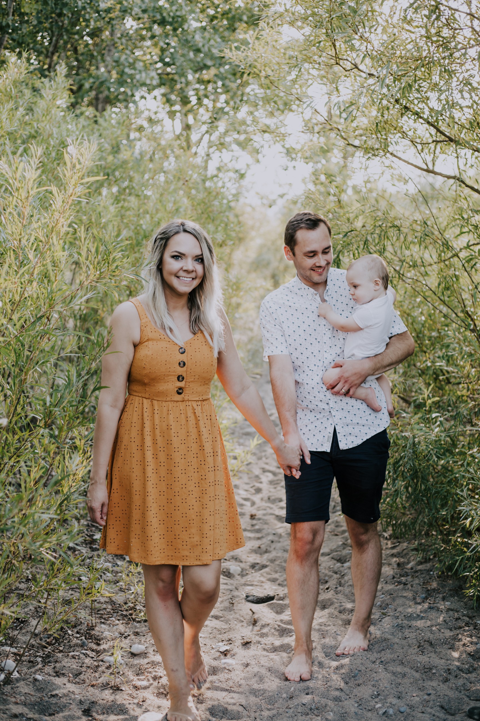 a young couple walks through the brush with their baby boy.