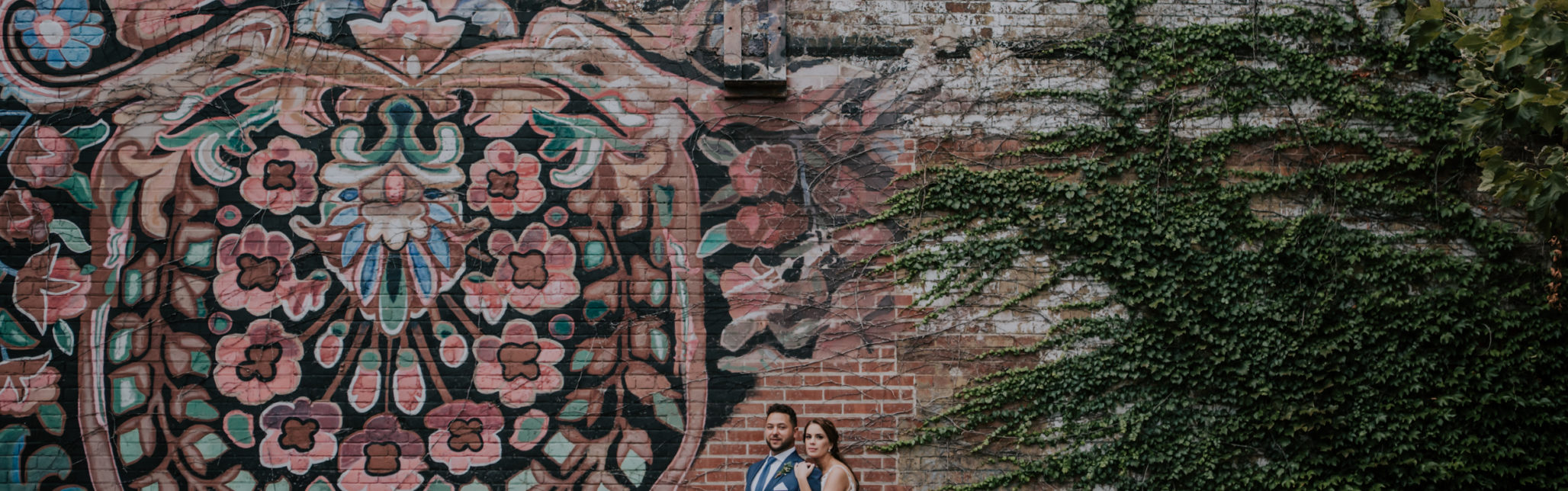 bride and groom standing against a graffiti brick wall
