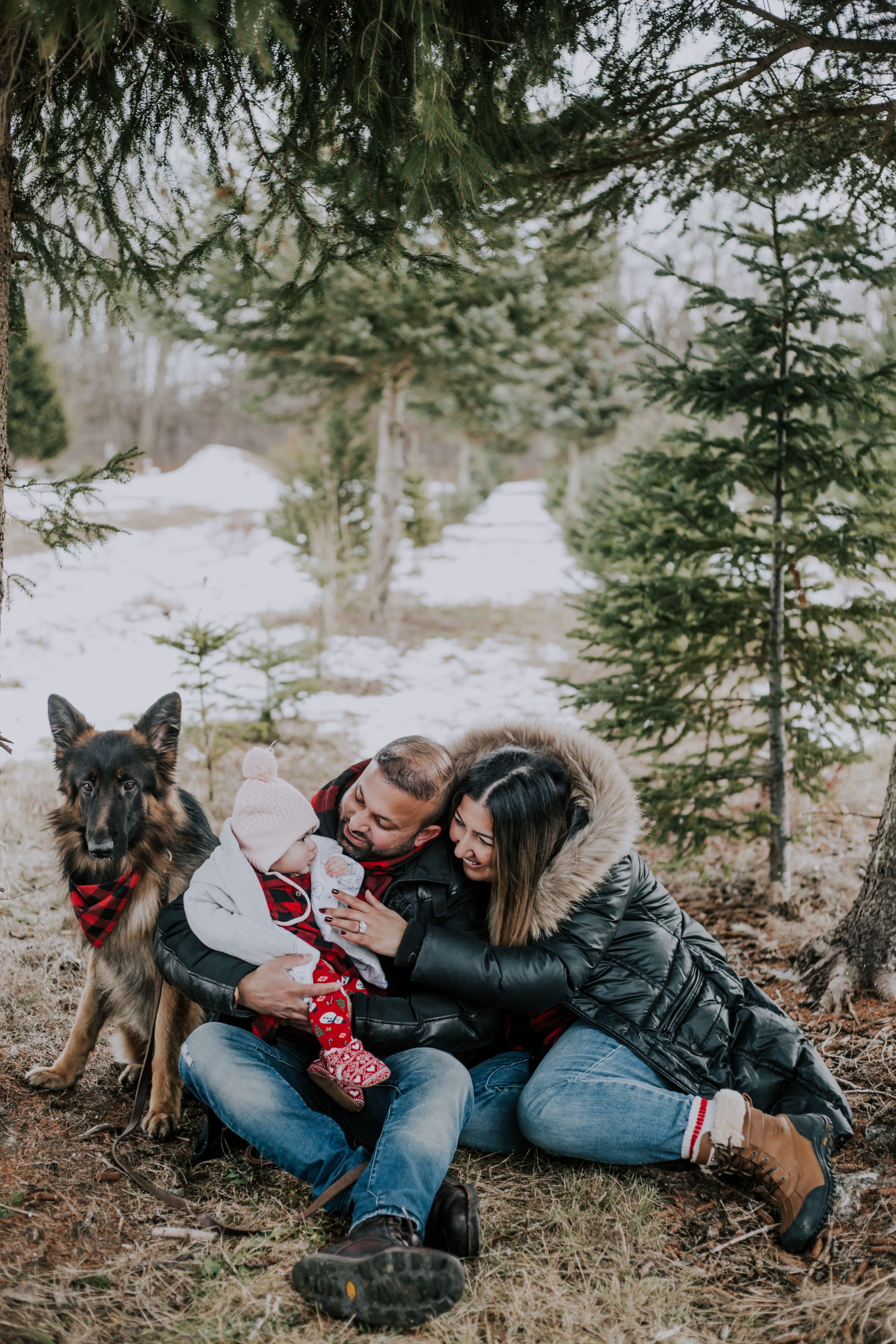 a couple embrace their baby daughter in the winter while sitting next to their dog