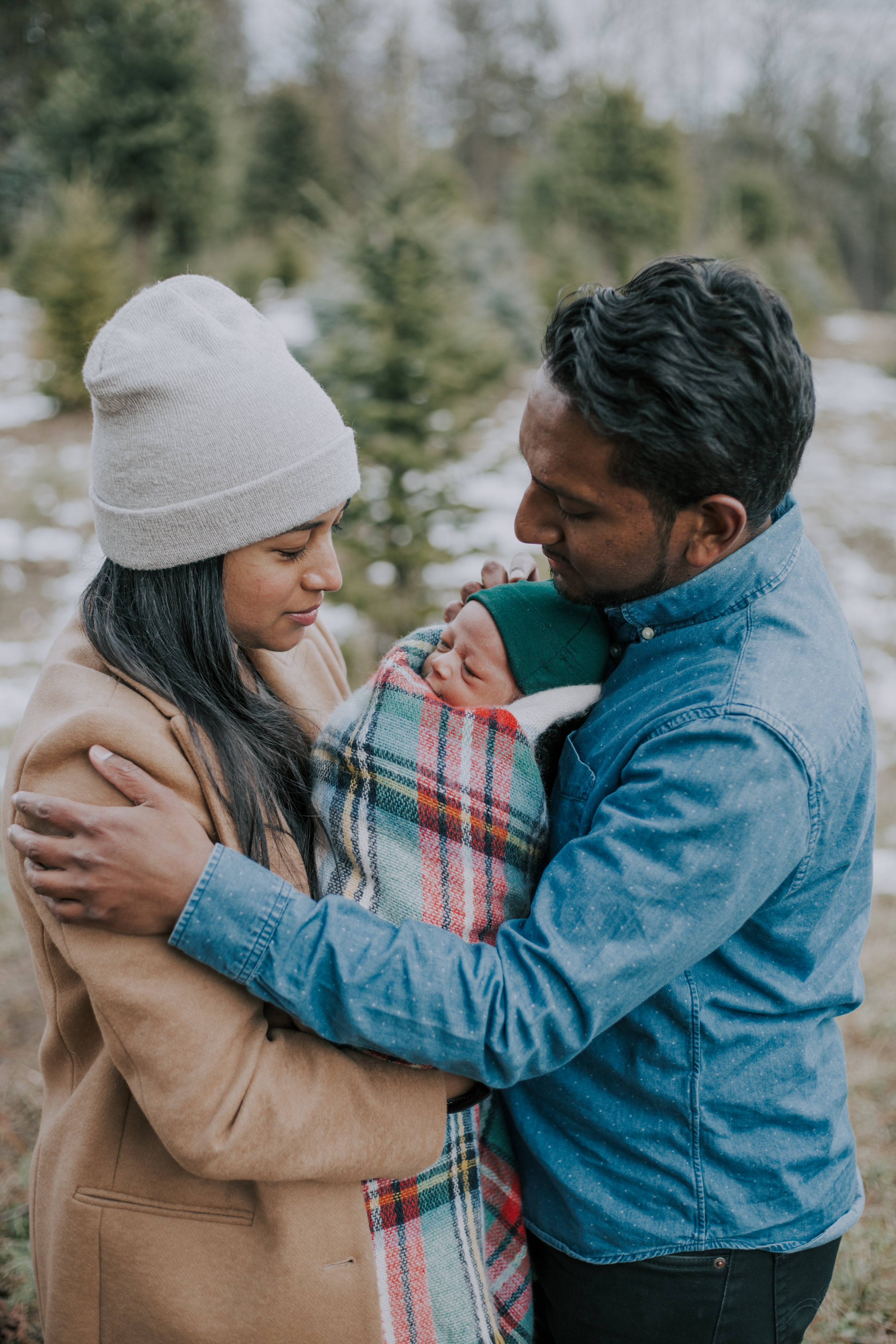 a young Indian couple hold their newborn son who is bundled in a plaid blanket 