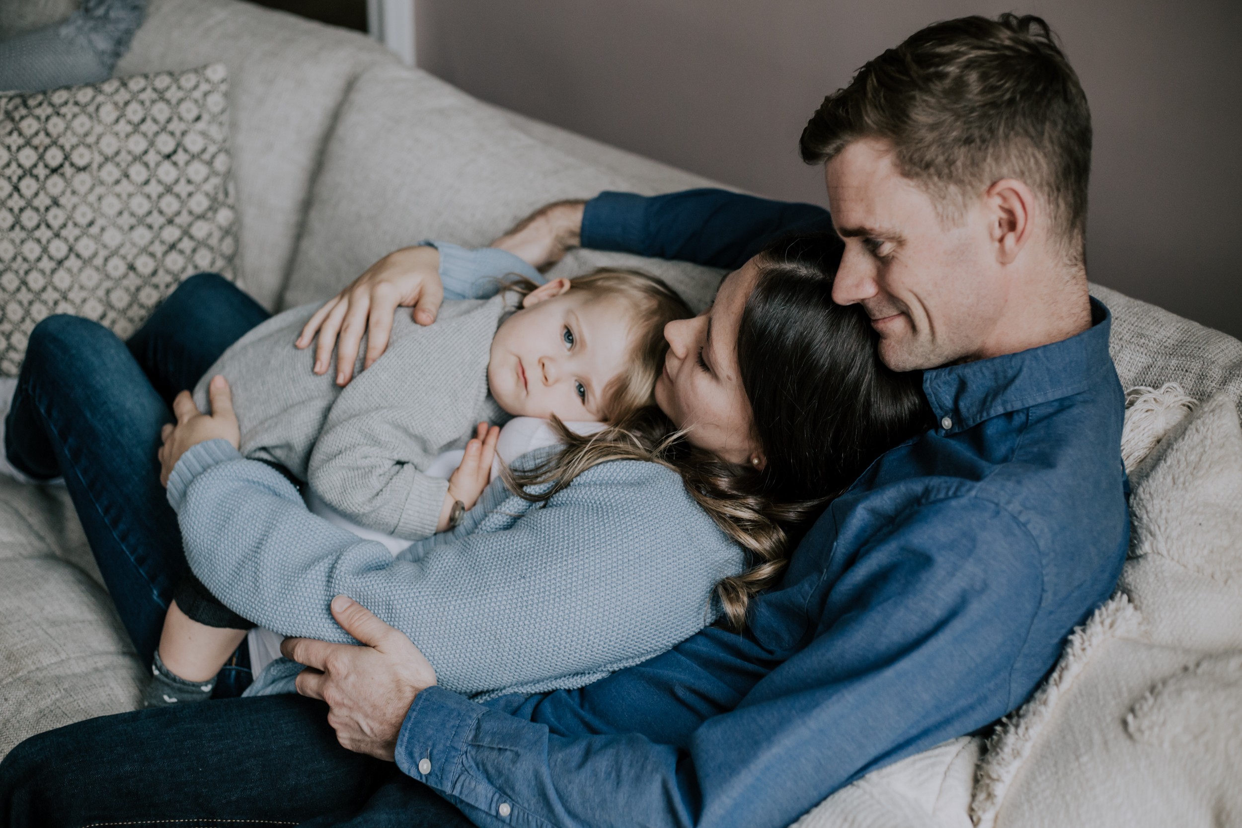a young couple embrace their toddler daughter on the sofa
