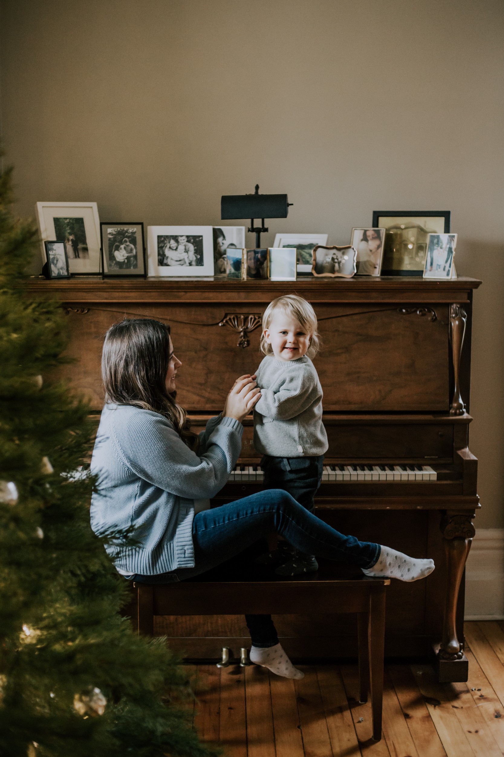 A mother sits on a piano bench holding the hands of her toddler daughter
