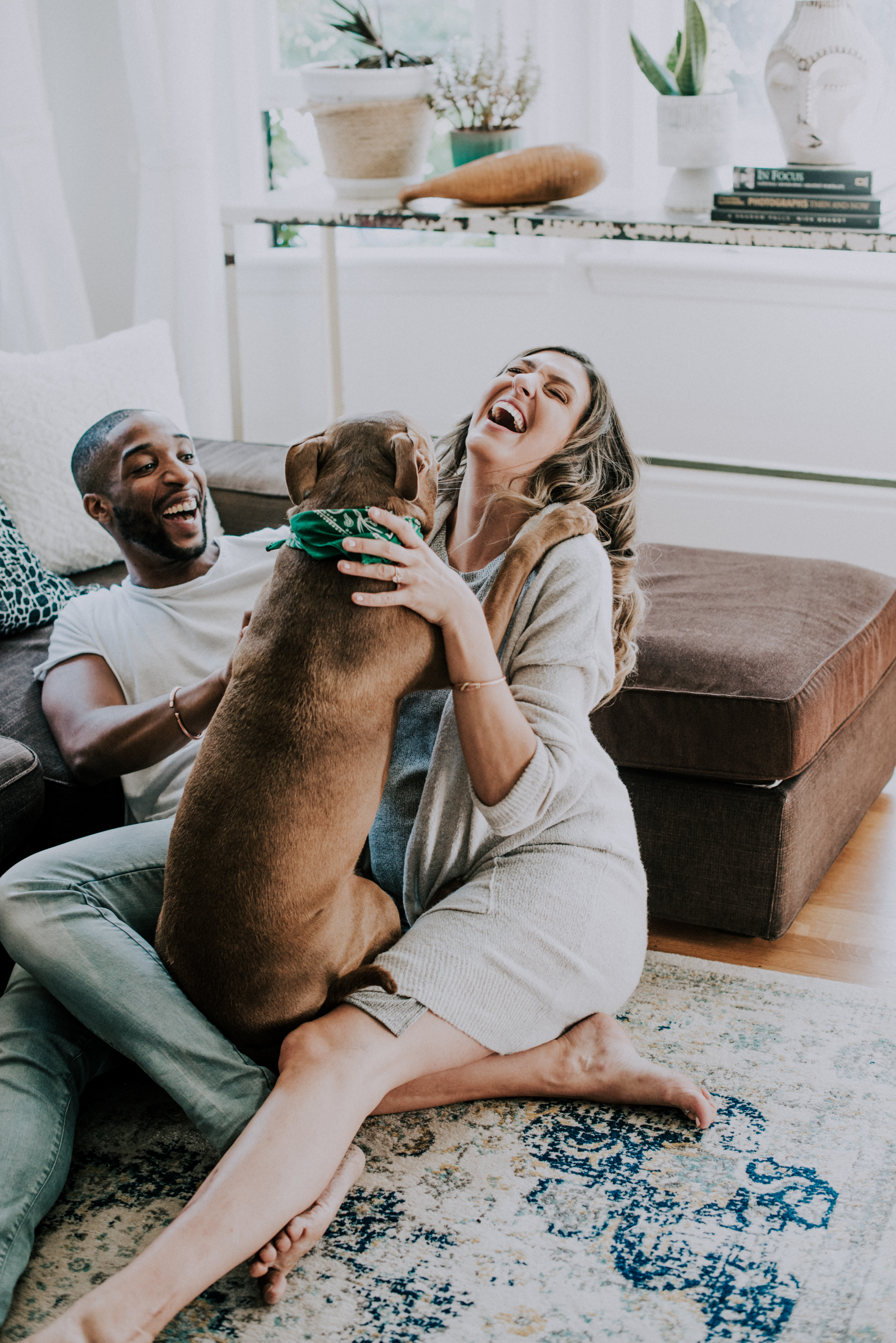 couple sitting on floor of living room while dog attempts to hug the pregnant woman