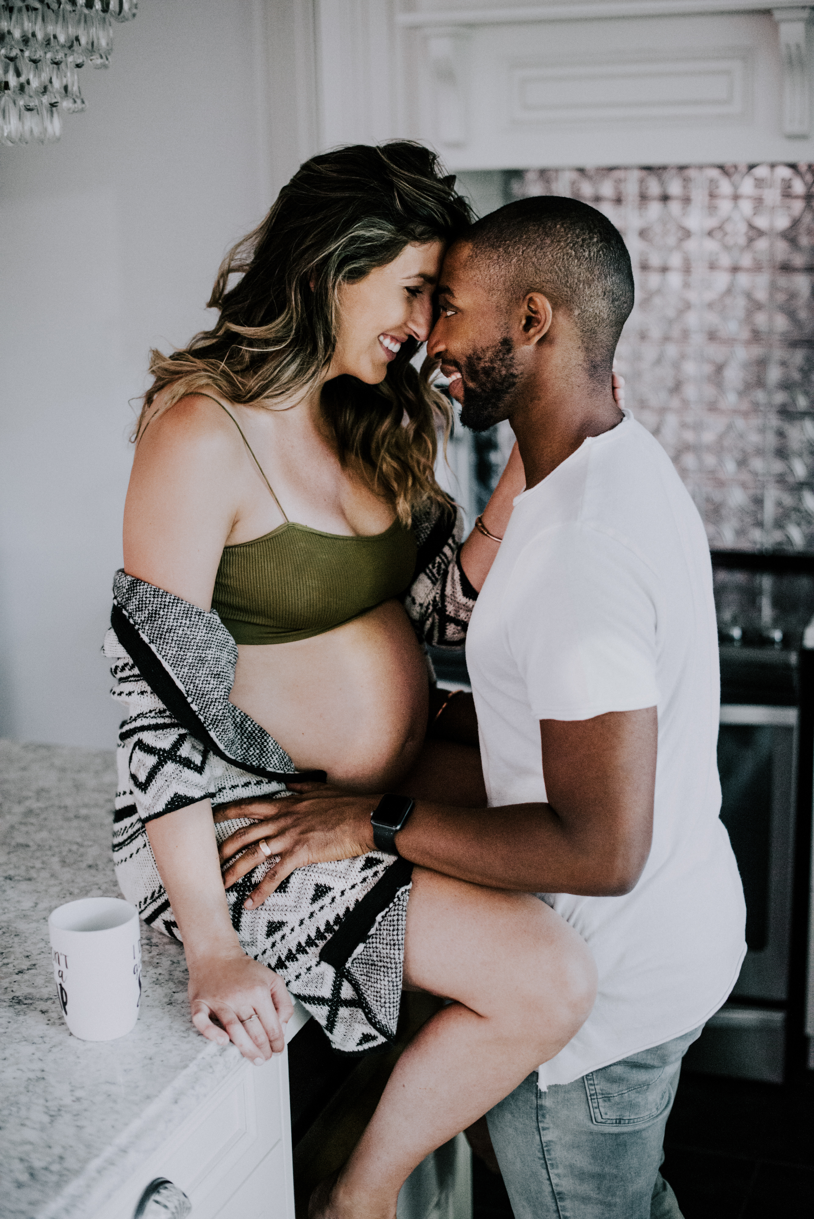 pregnant woman sits on kitchen island with husband smiling resting his forehead on hers
