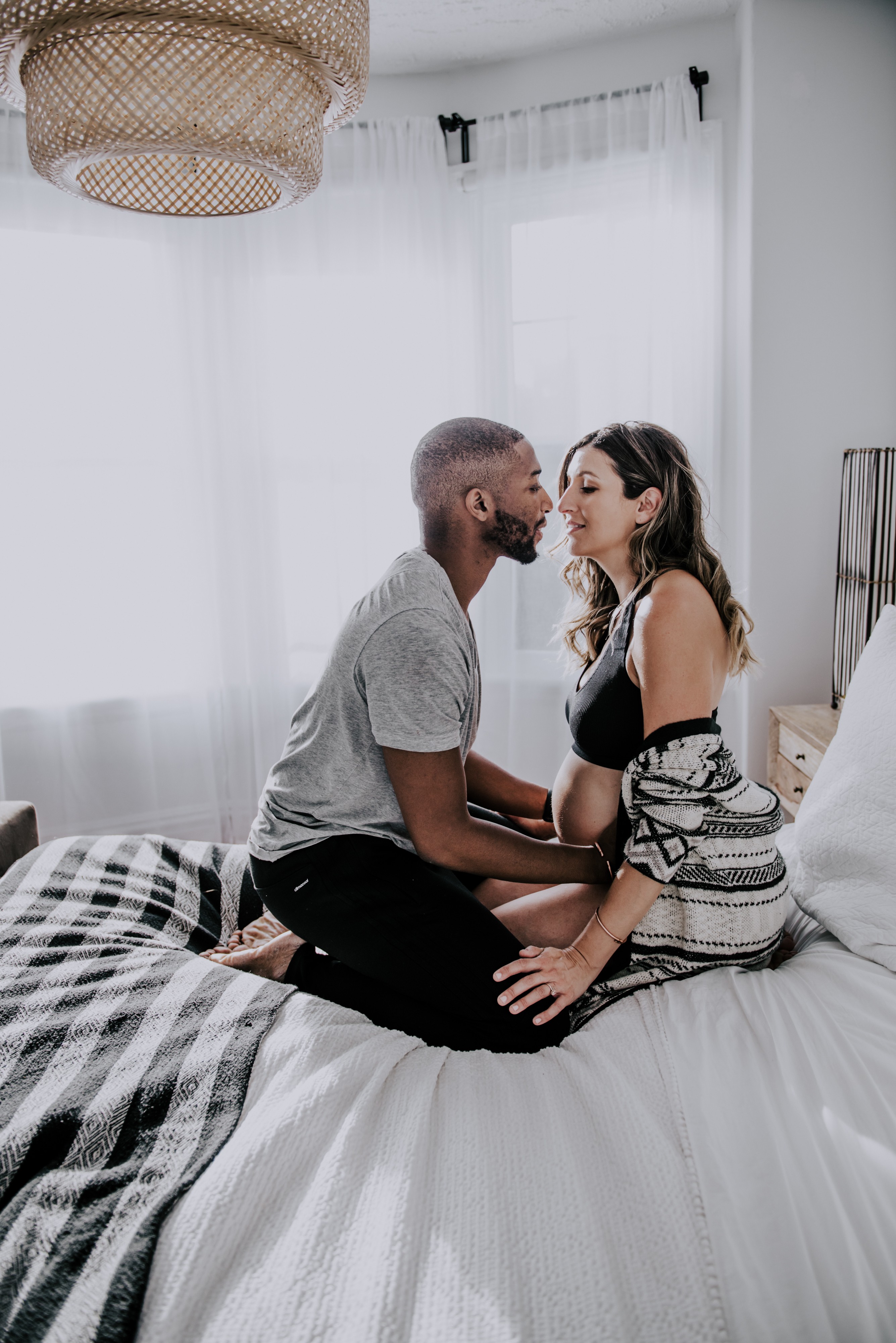 a couple sit on knees while kissing on their bed