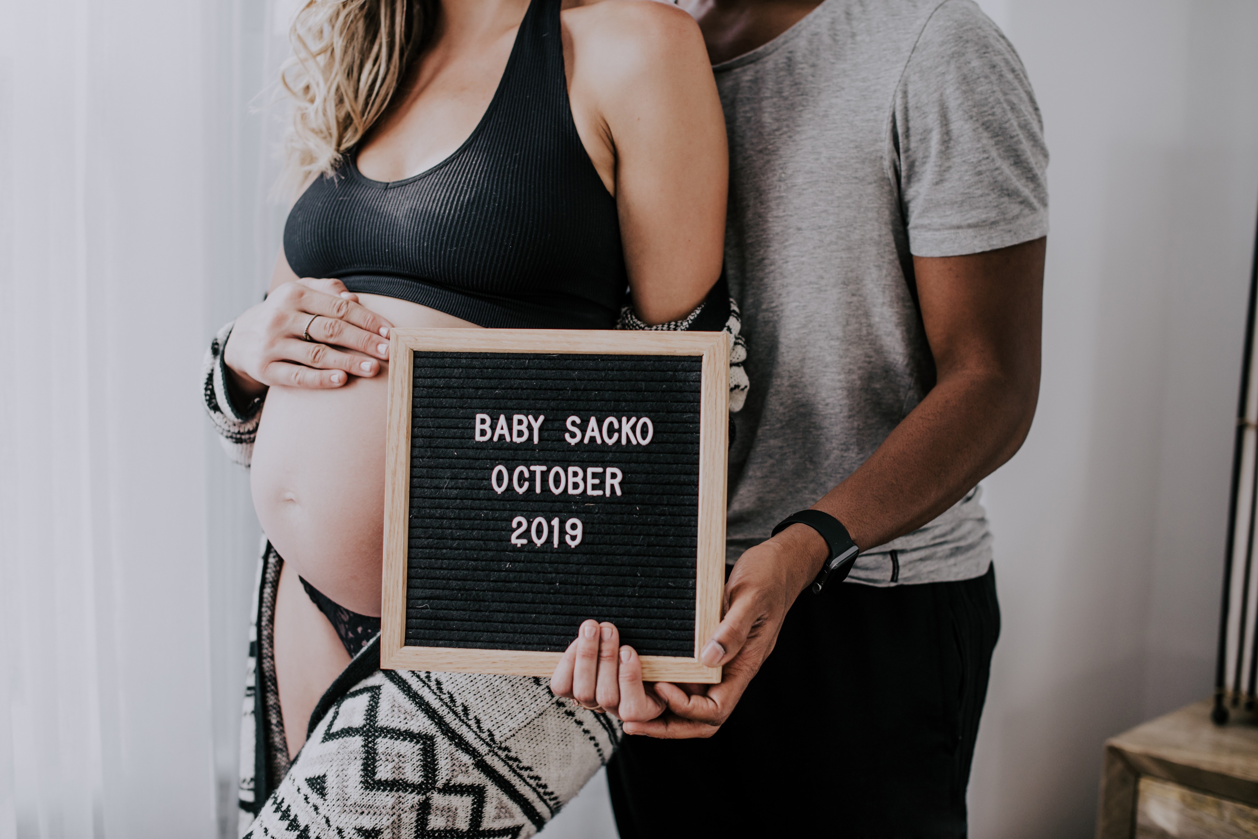 maternity photo of woman's belly and partner embracing her from behind