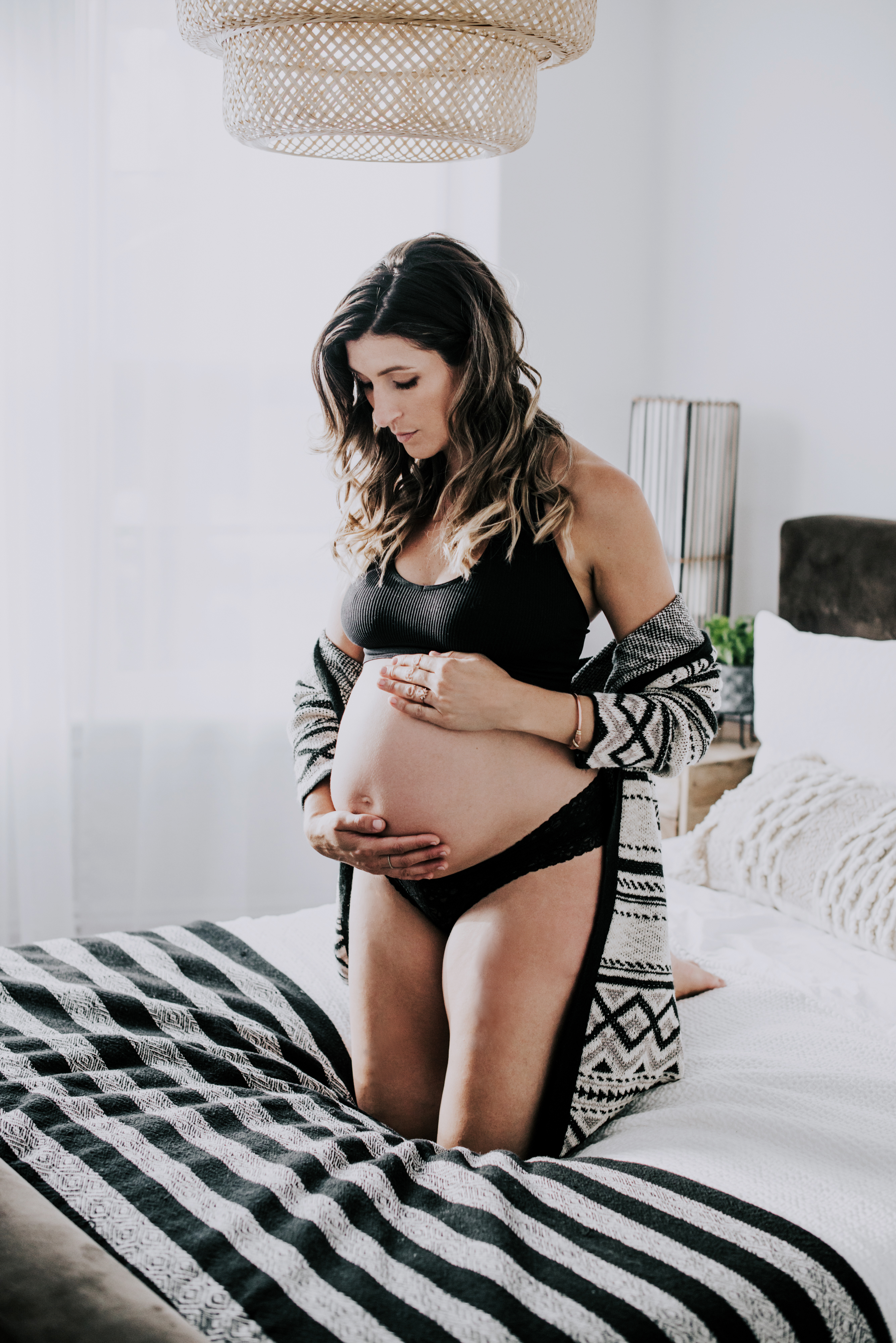 pregnant woman kneels on bed touching her bare belly
