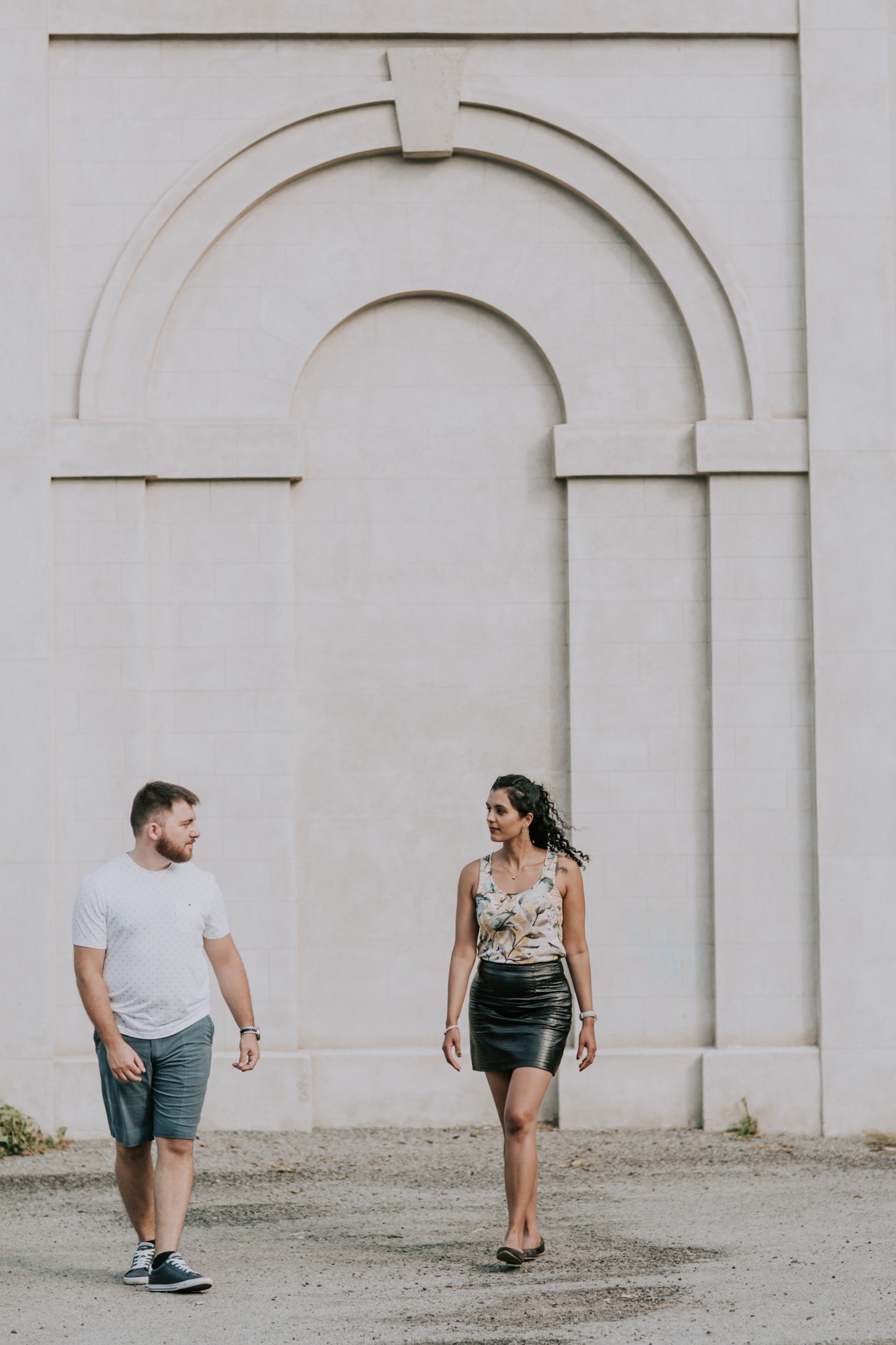 couple walks in front of white brick wall
