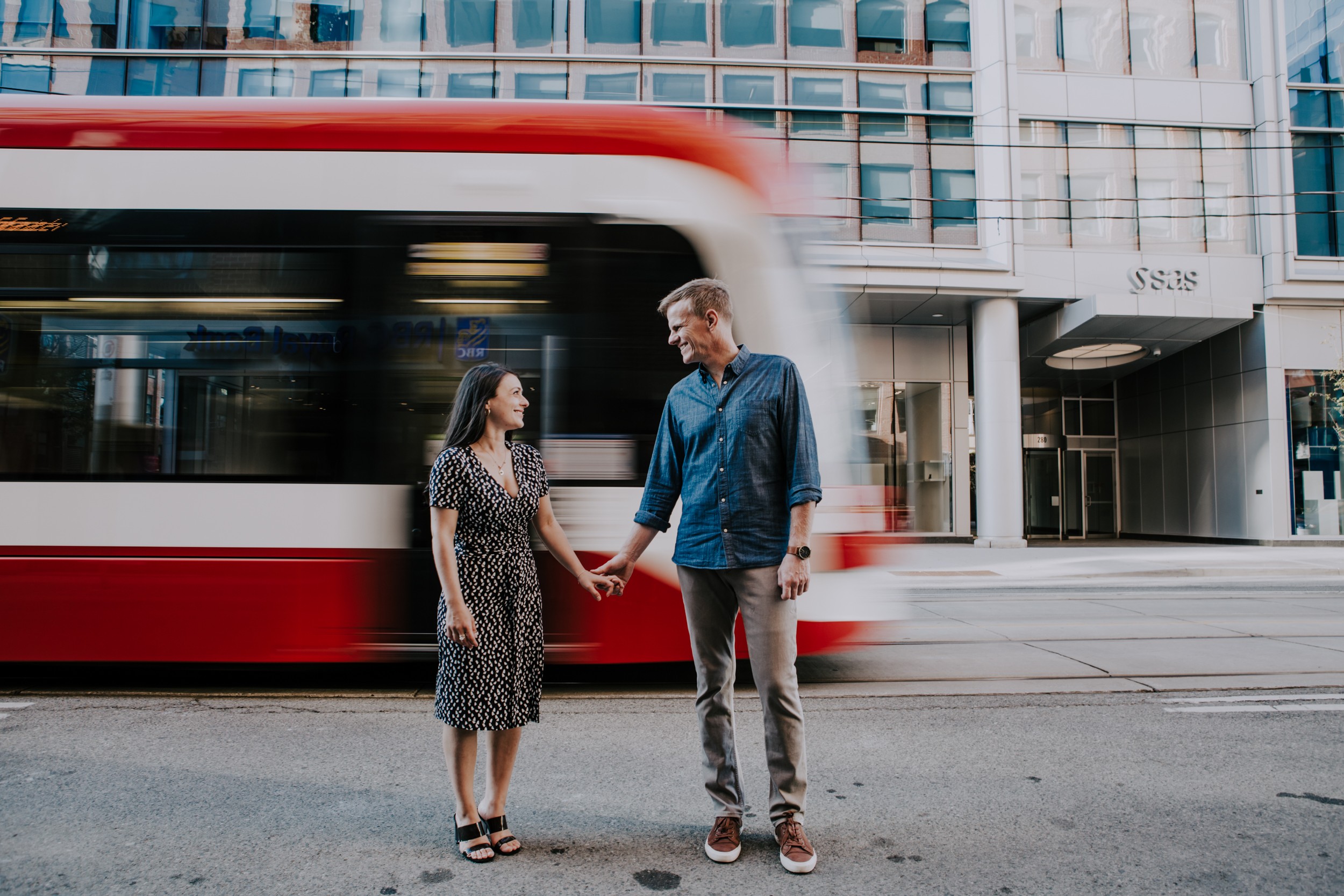 couple hold hands while standing on street and toronto street car blurs by
