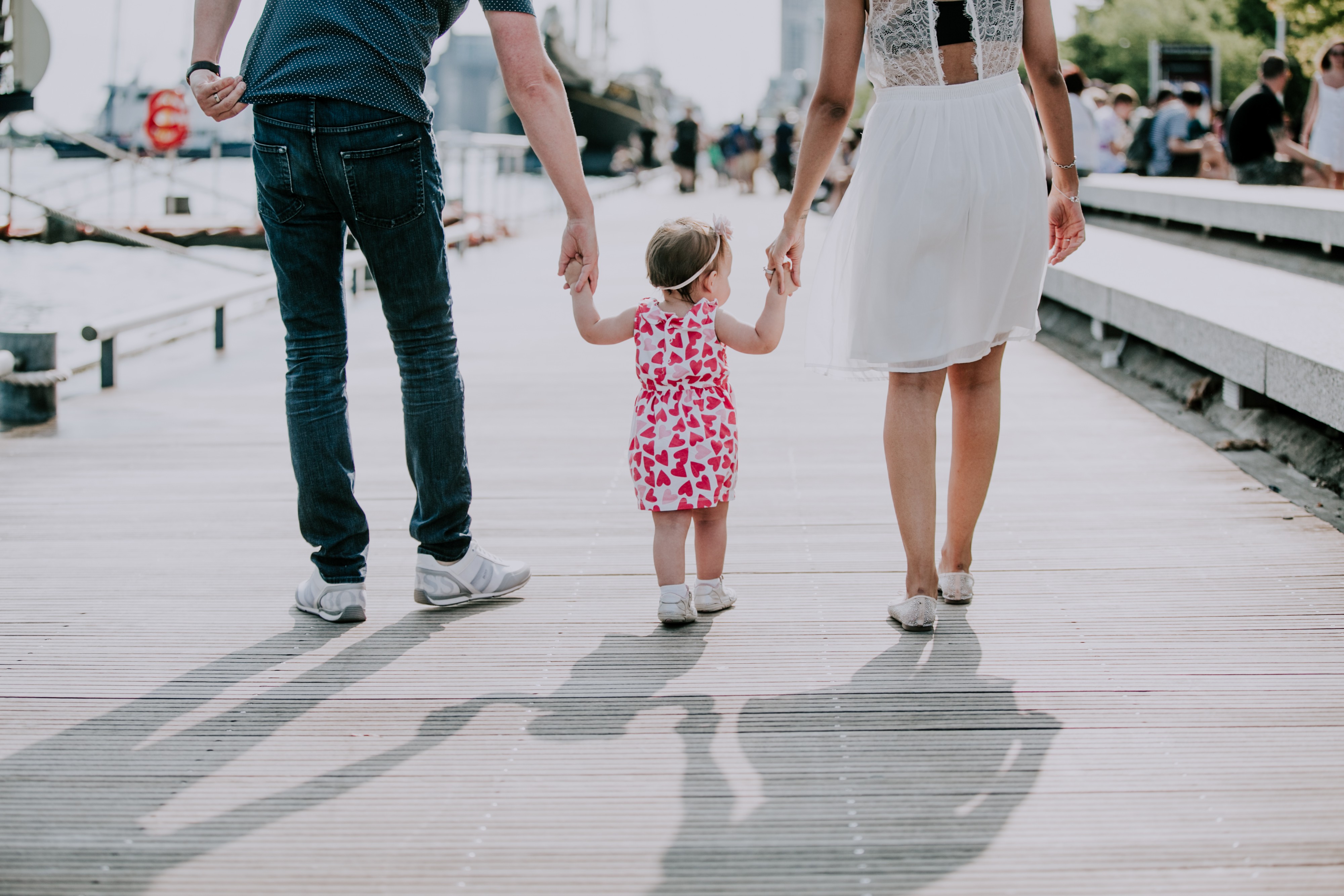 mother and father walk with toddler while holding her hands