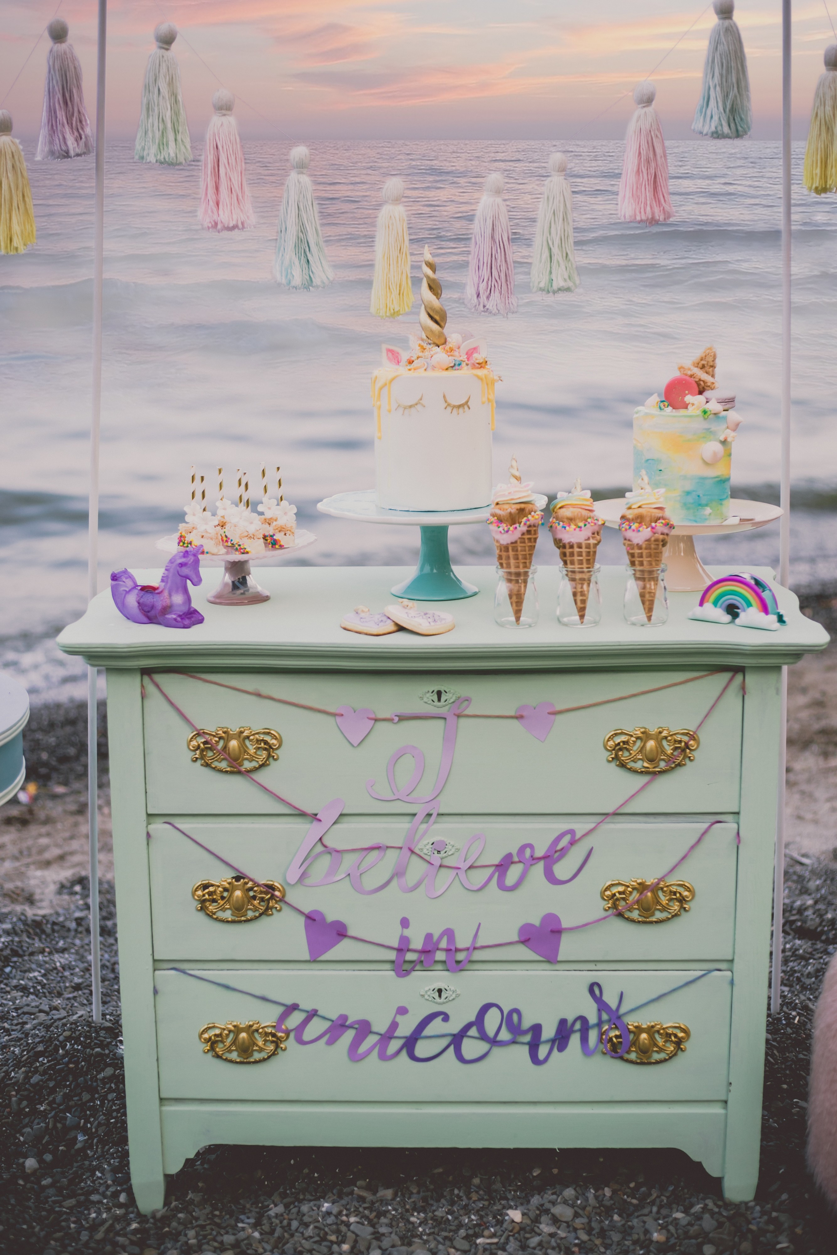 unicorns themed dessert table spread on mint green dresser with unicorn cake on top