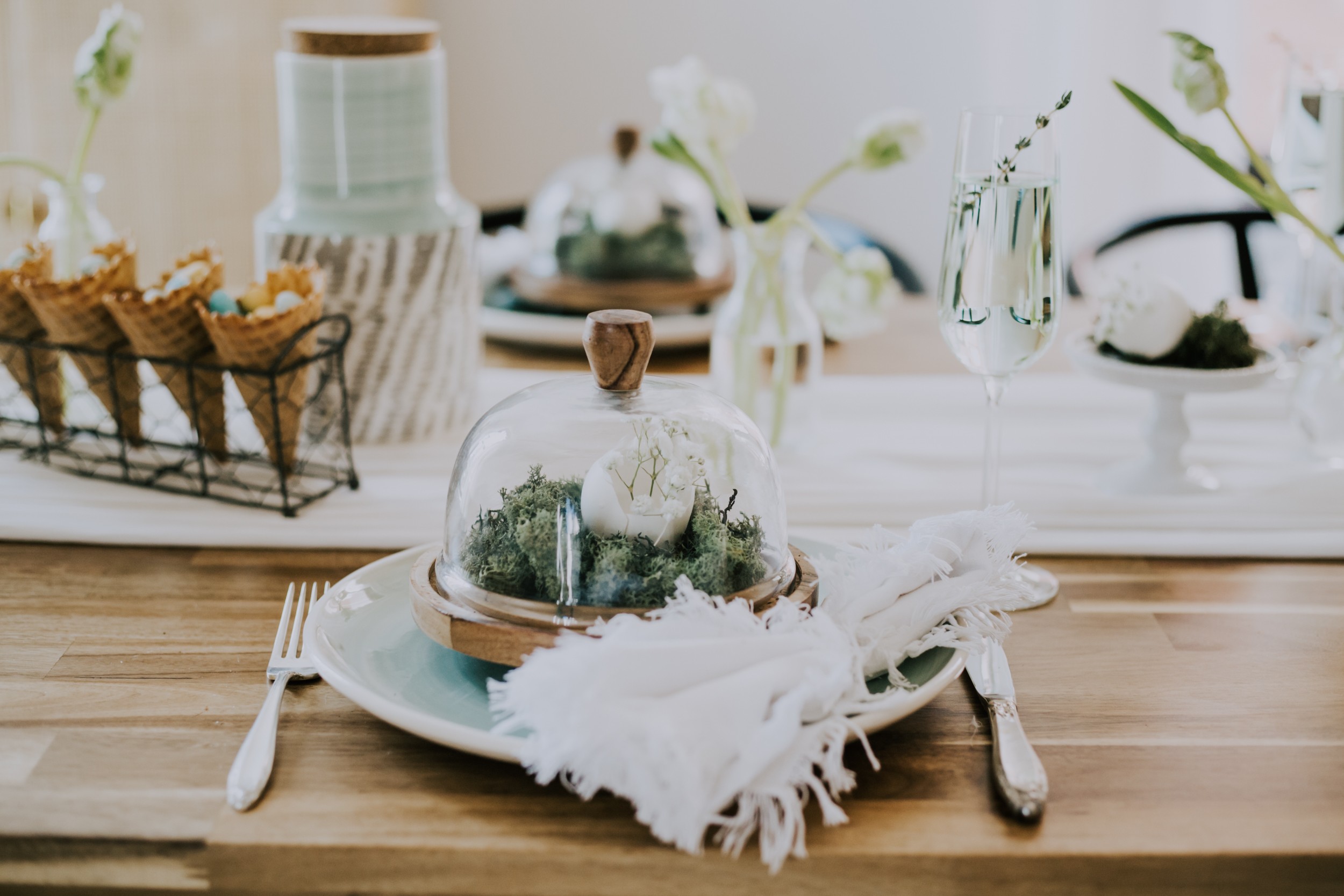 Organic and elegant easter tablescape decor. Teal plates with antique silverware, wooden globes filled with moss and a cracked egg filled with white flowers. 