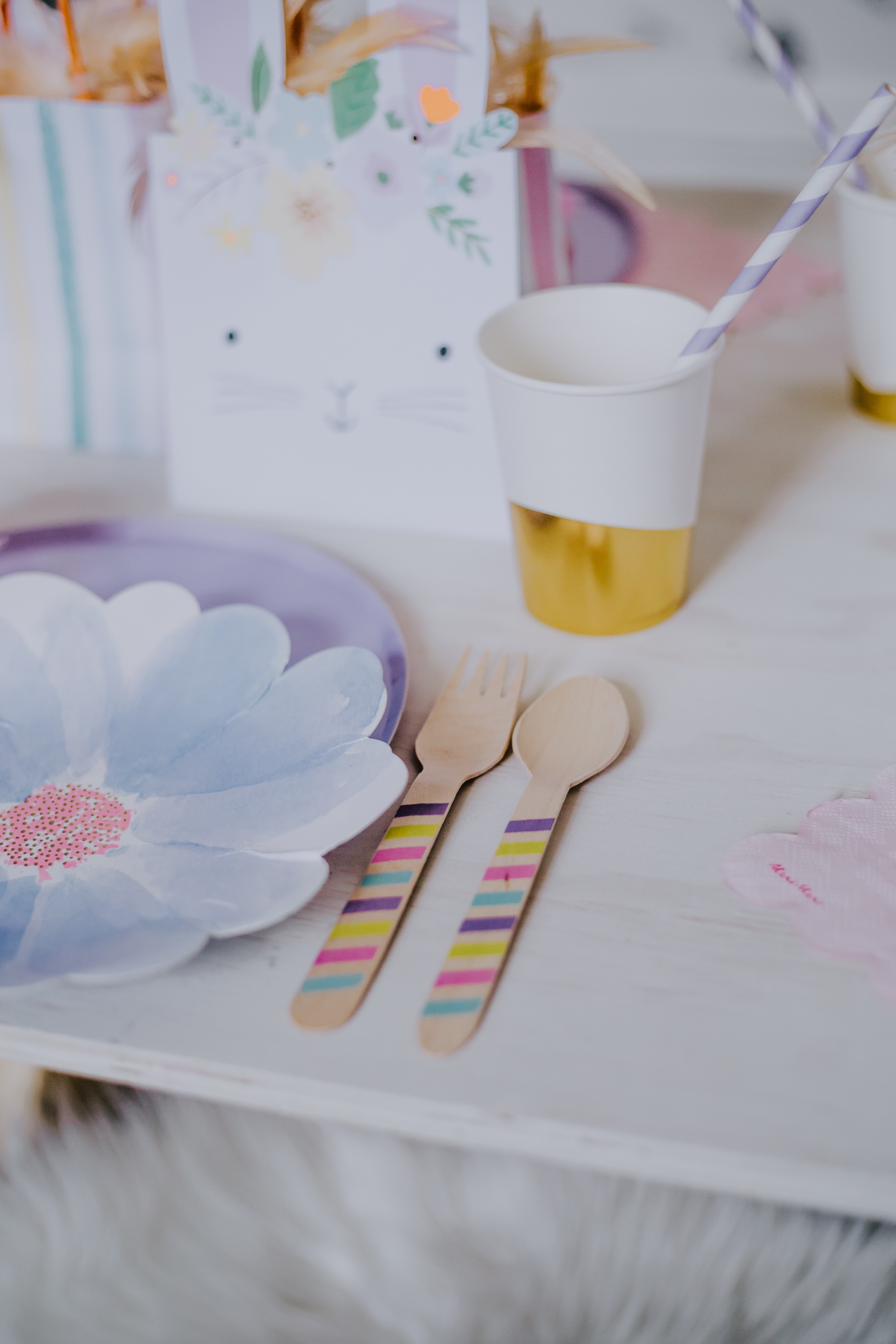 multi coloured wooden cutlery sits next to flower paper plate for an easter kids table