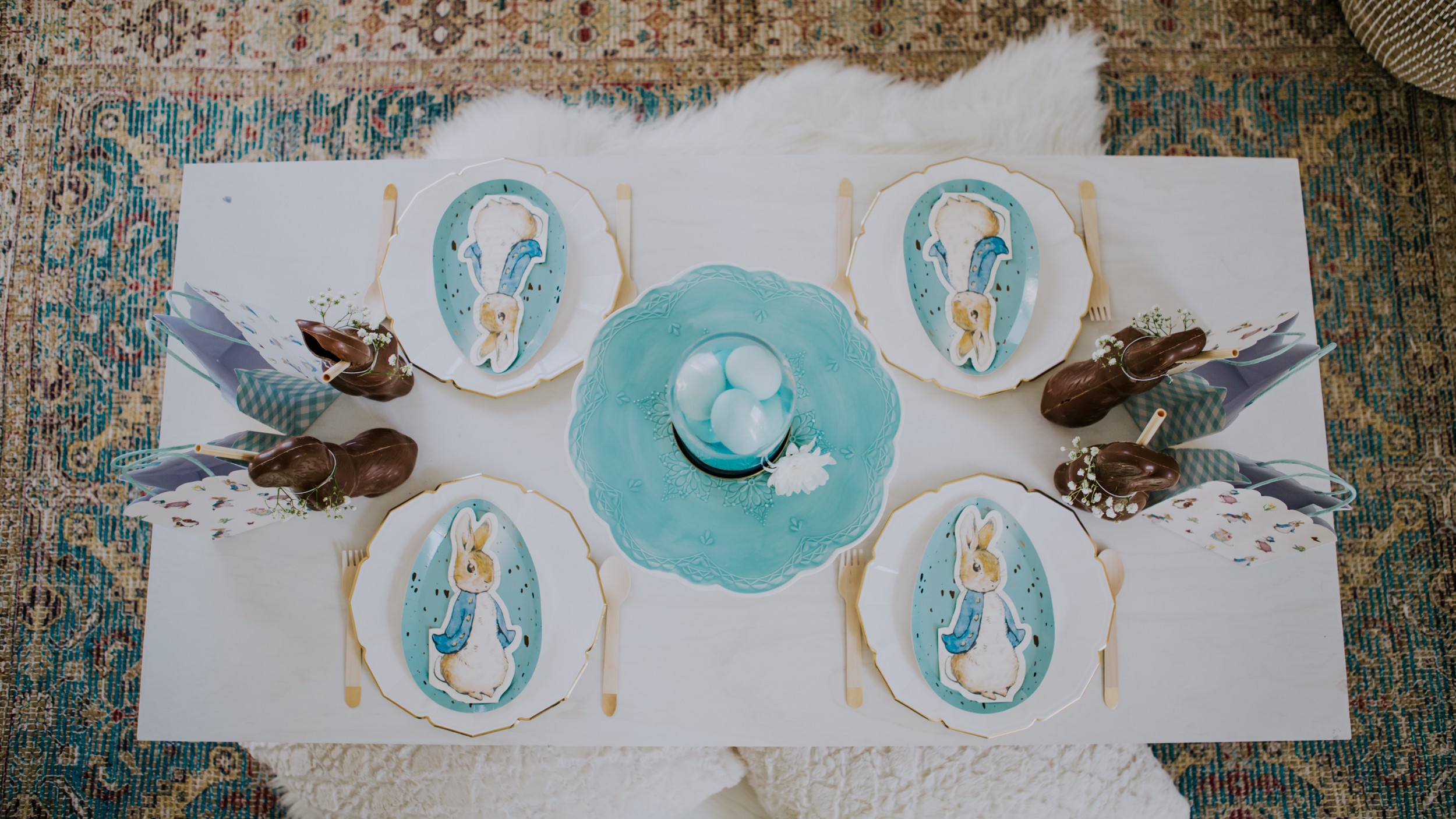 4 place settings at a white table with Peter Rabbit napkins, blue easter egg plates and blue eggs in the centre of the table